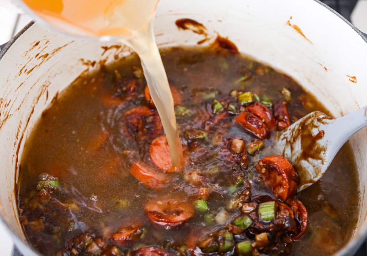 Someone pouring chicken broth into the roux mixture and seasonings.