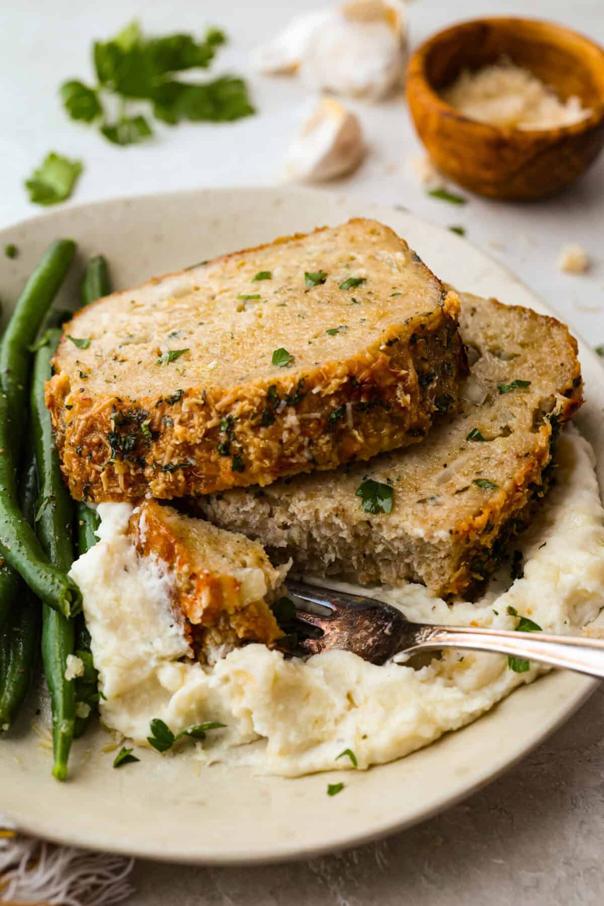 Plated slices of garlic parmesan chicken meatloaf with mashed potatoes and green beans. 