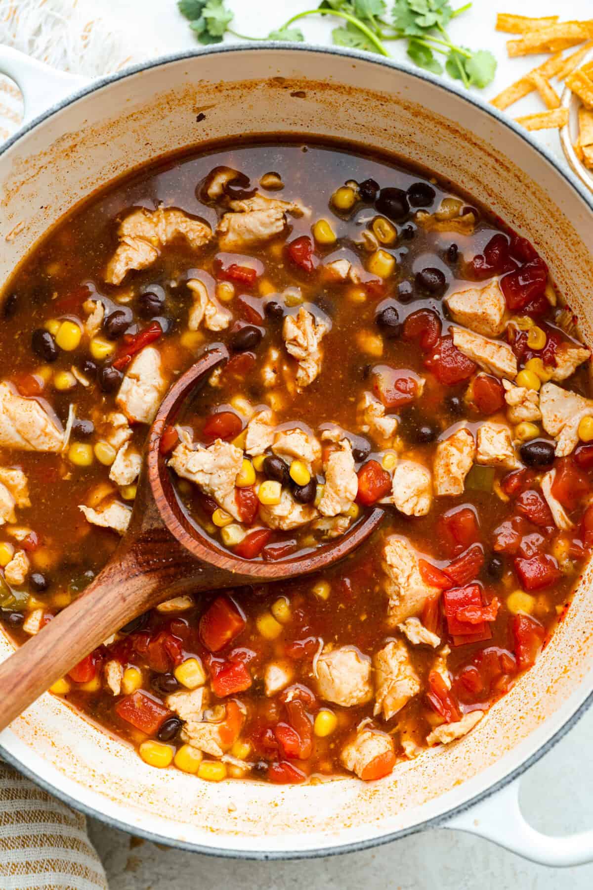 Pot of 8 can chicken tortilla soup with a wooden ladle.