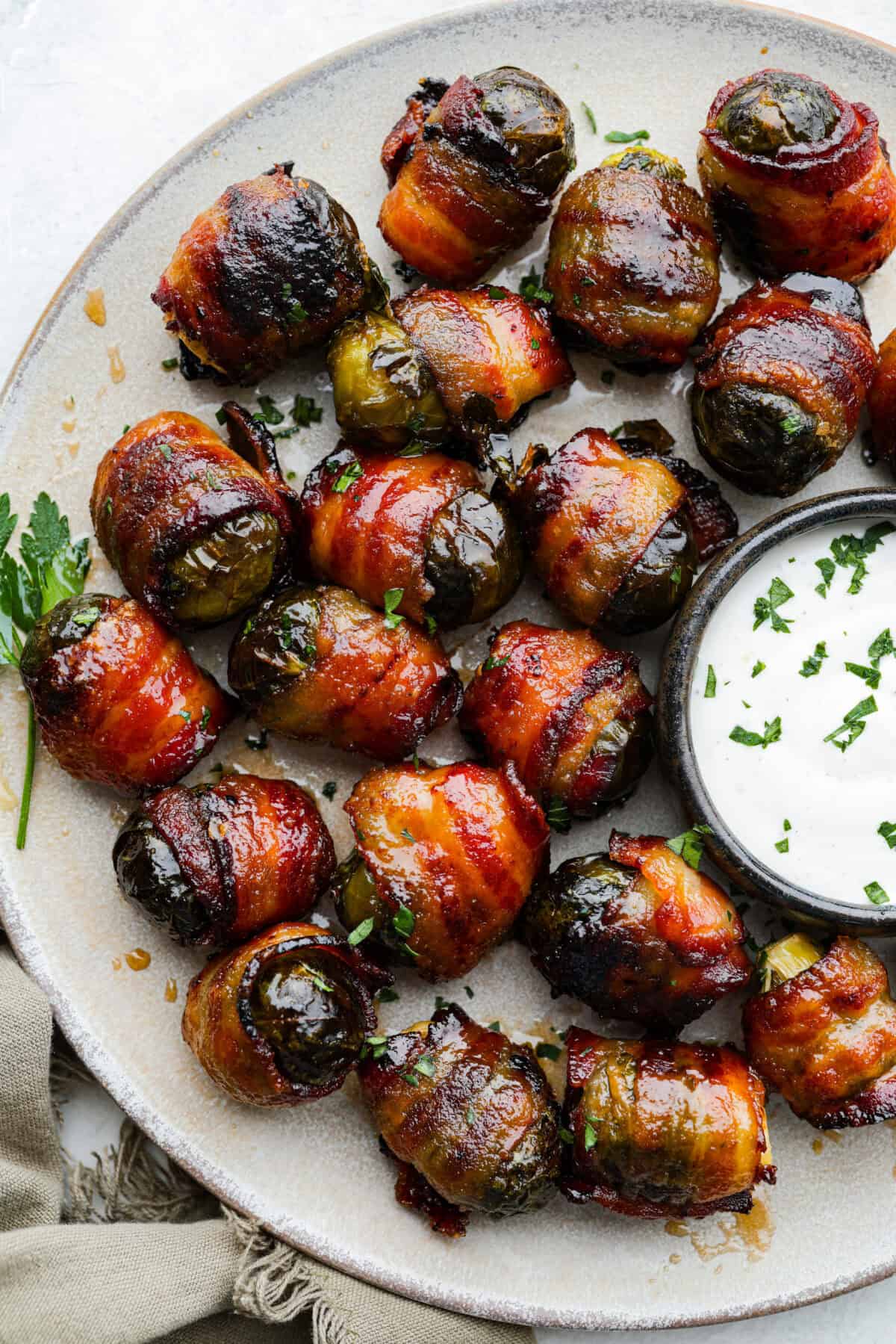 A platter of bacon wrapped Brussels sprouts with some dip. 