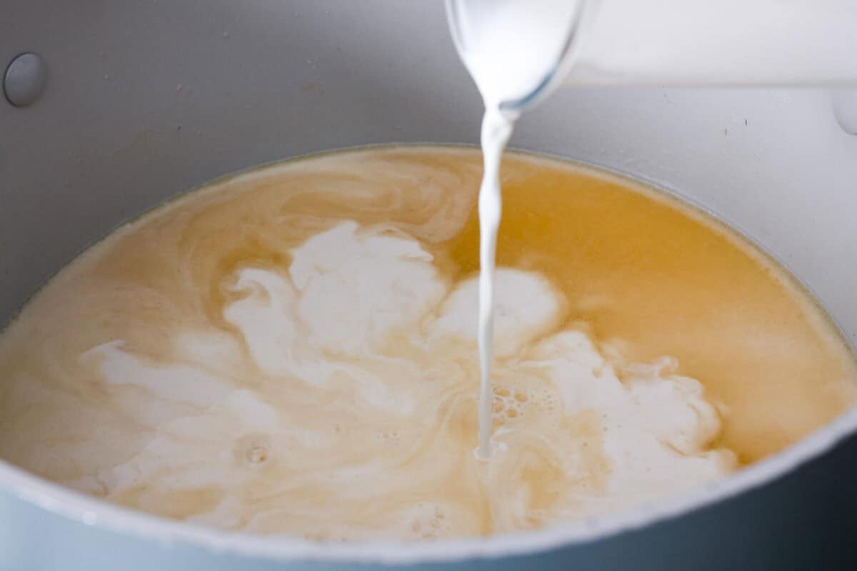 Someone pouring half and half into the chicken stock.
