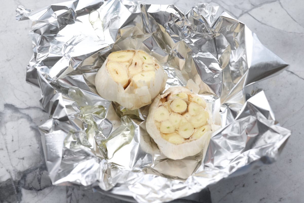 two garlic bunches with tops cute off in tin foil ready to be roasted. 