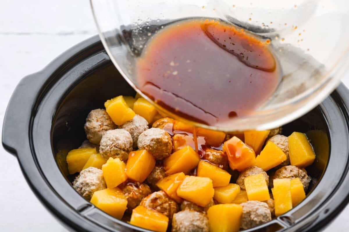 Mixed sauce being poured over the meatballs and pineapple. 