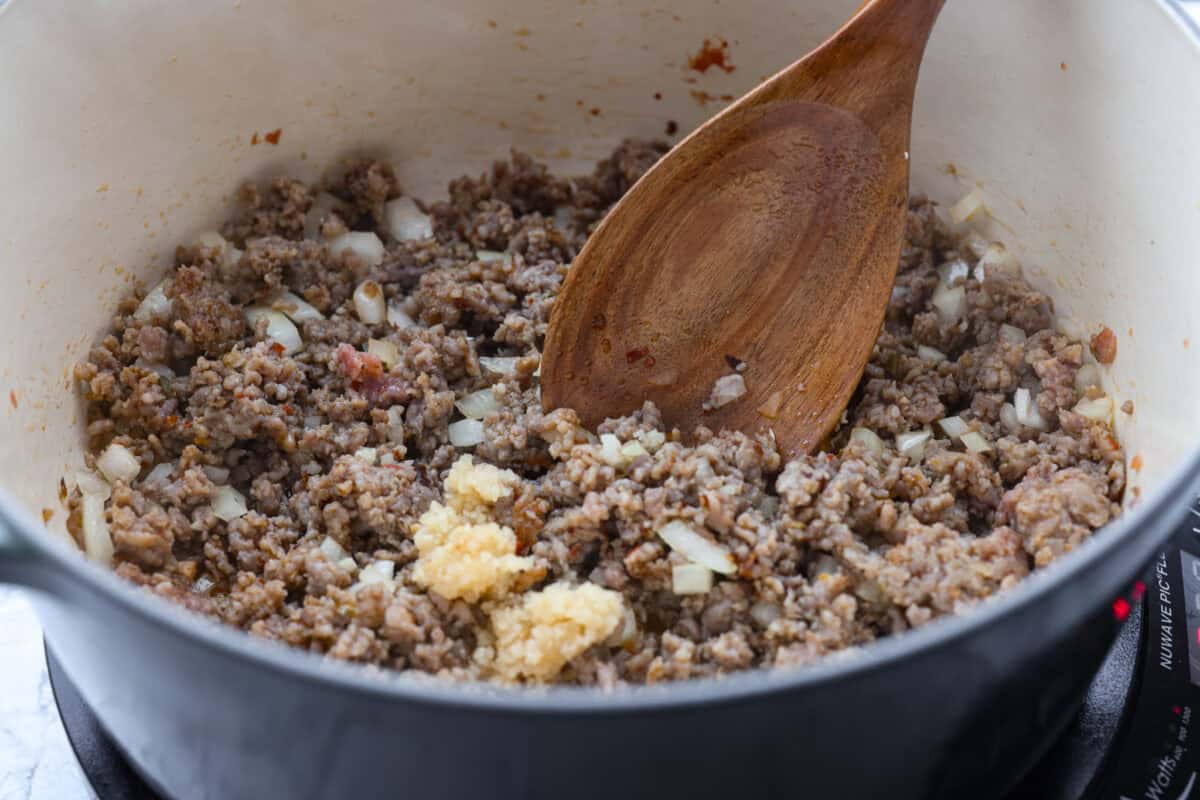 Italian sausage, onion, and garlic cooking in a pot.
