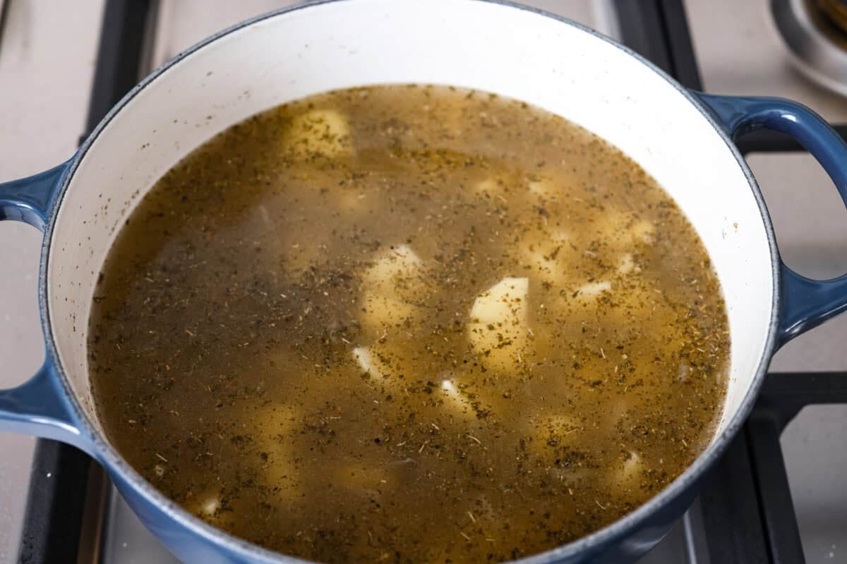 Chicken broth, potatoes, and seasonings added to the pot with shallots. 