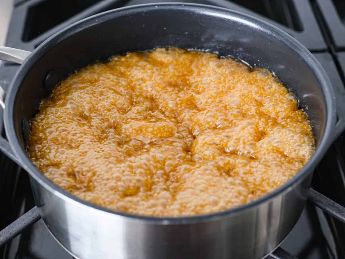 Toffee ingredients boiling in a pot on a stove.