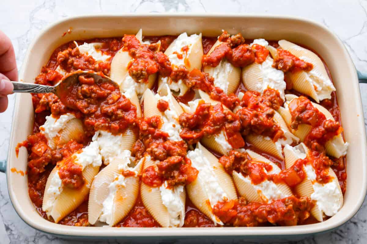 Someone spooning more marinara mixture to the top of the million dollar stuffed shells. 