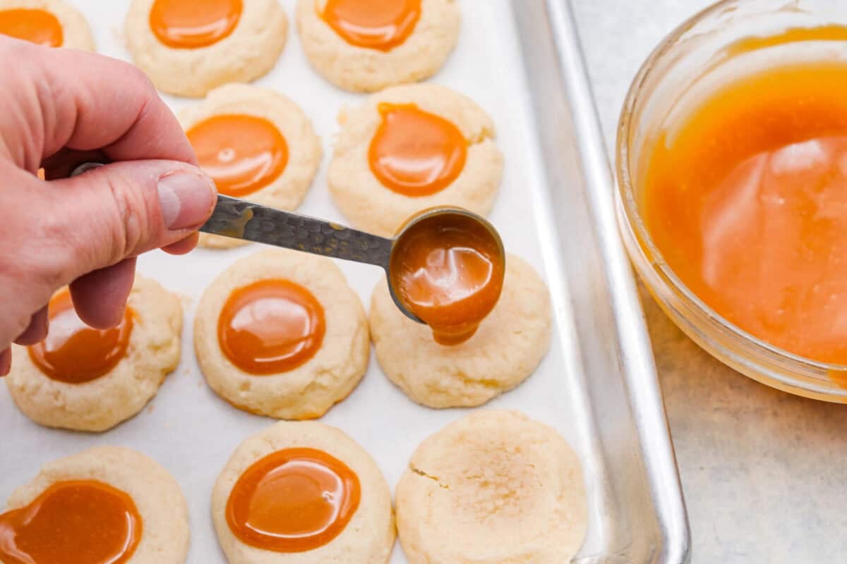 Someone spooning a small amount of caramel into the thumbprint well in the cookie. 