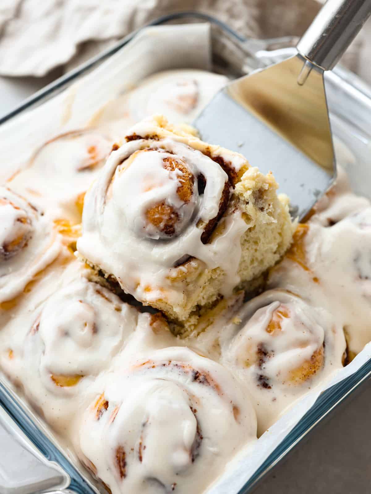 Someone lifting a cinnamon roll our of a baking dish. 