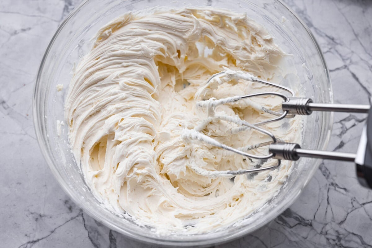 Frosting ingredients being whipped with a hand mixer until fluffy. 