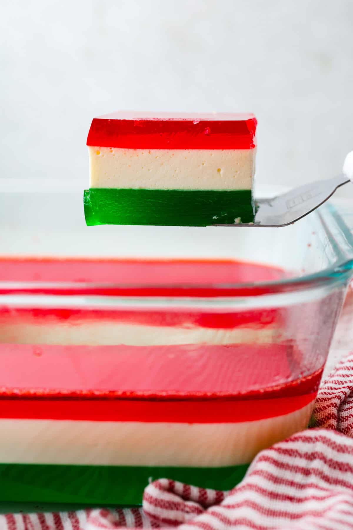 Someone lifting a serving of Christmas ribbon salad out from the baking dish. 