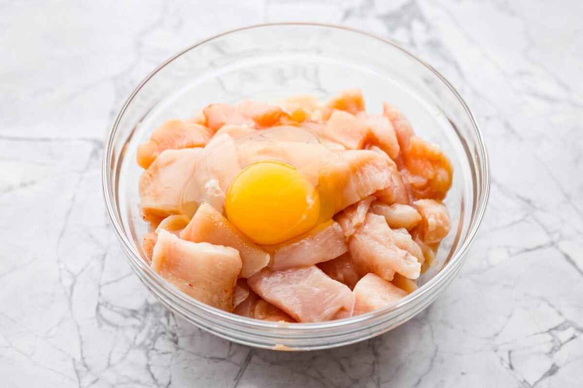 Bowl of seasoned chicken with a cracked egg on top. 