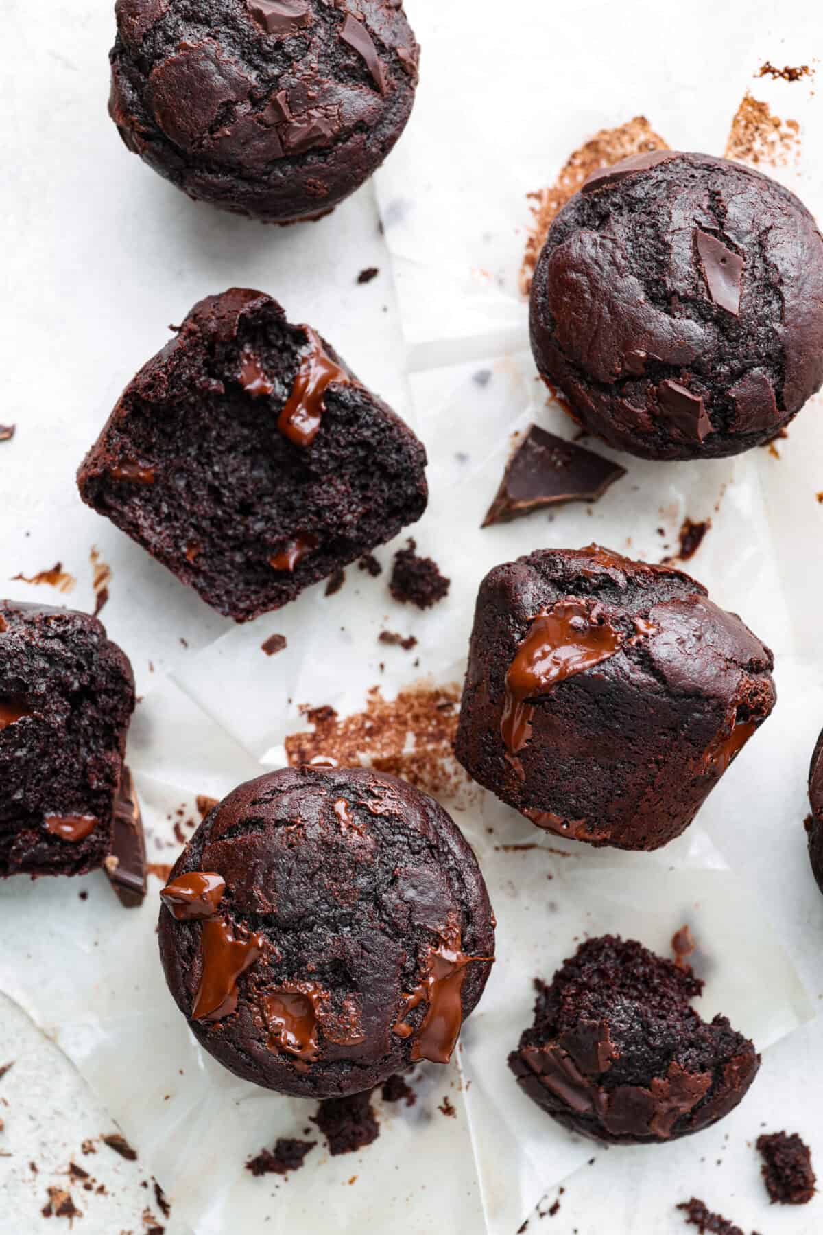 Overhead shot of double chocolate muffins scattered on parchment paper.