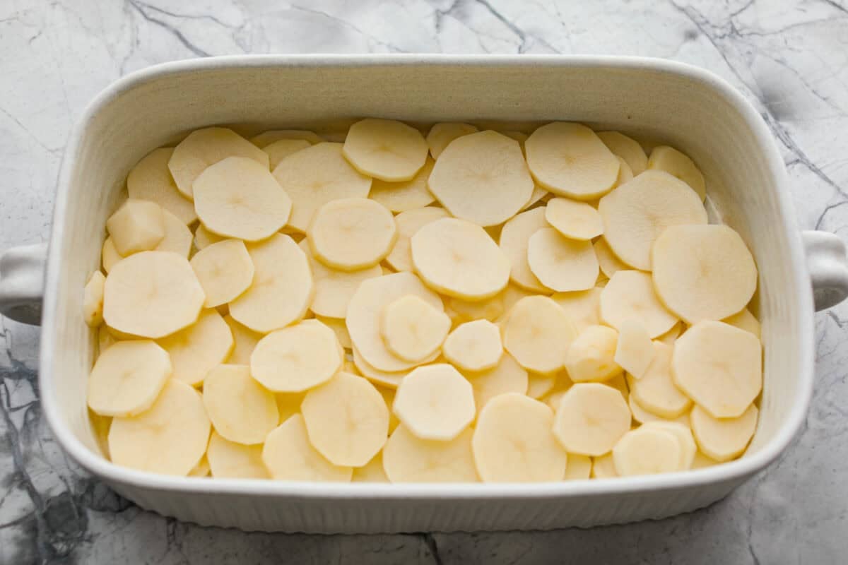 Sliced potatoes layered on the bottom of the baking dish. 