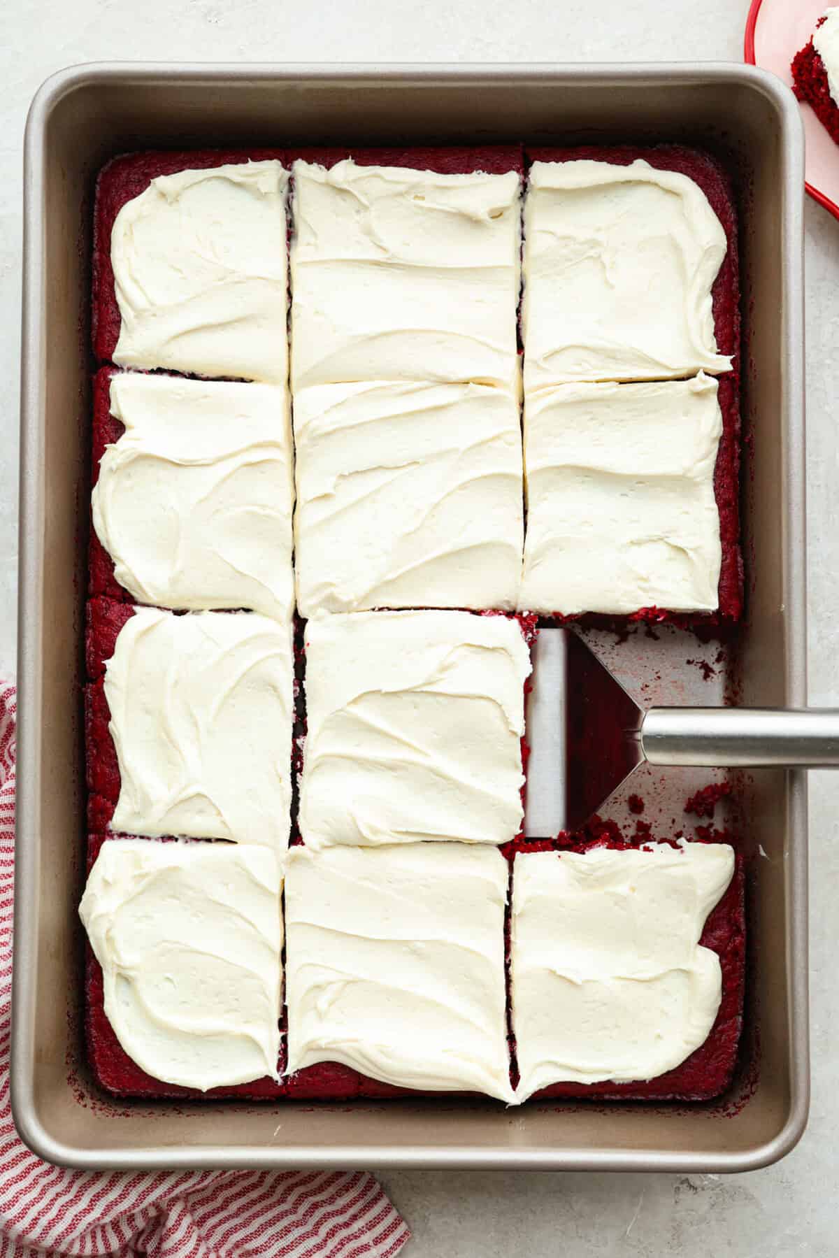 Overhead shot of the 2 ingredient red velvet cake frosted, sliced and someone using a spatula to lift a piece out. 