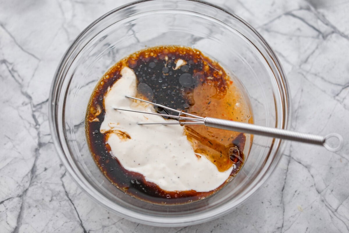 Sauce ingredients added to a mixing bowl with a small whisk.