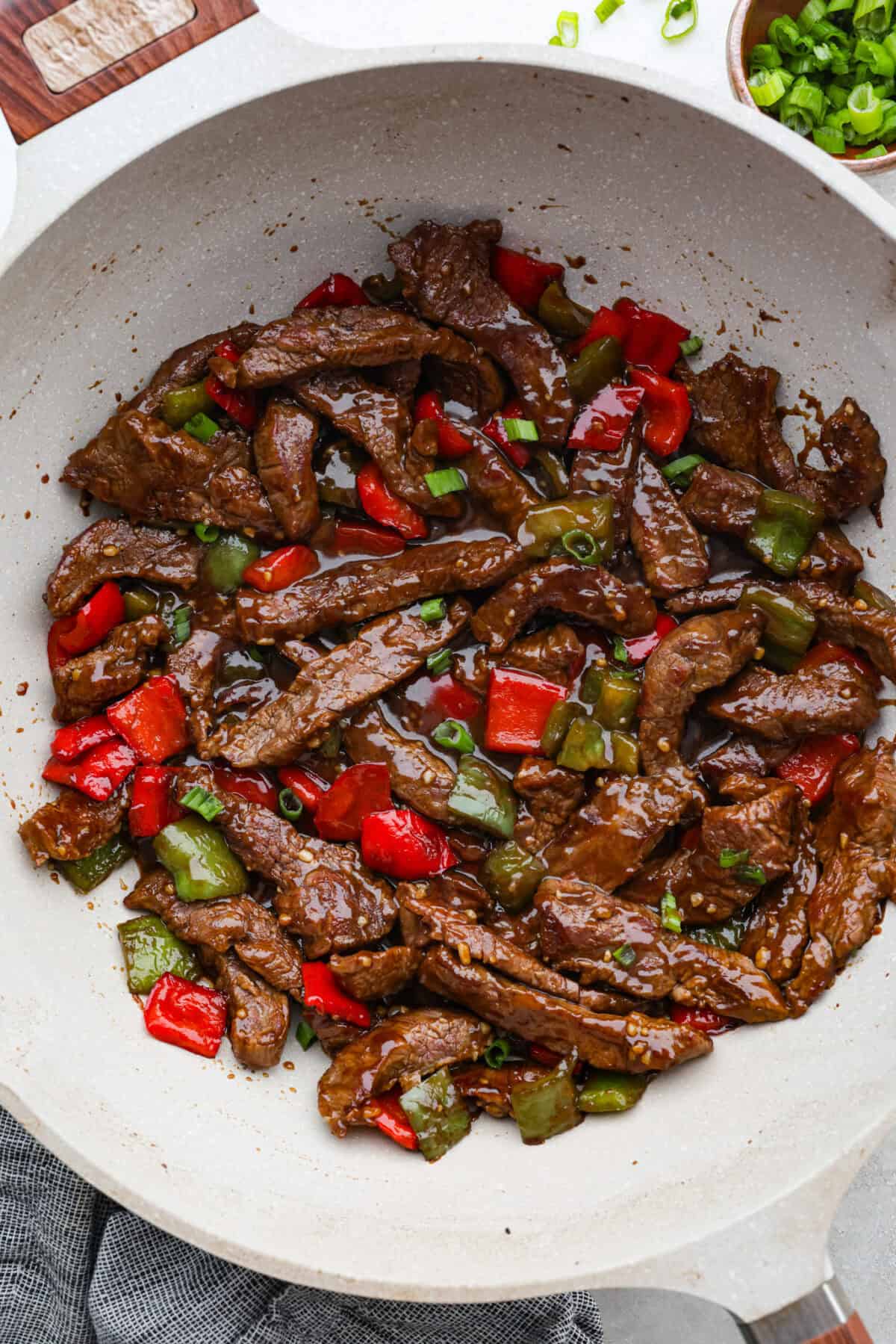 Overhead shot of pepper steak completely cooked and in the wok garnished with green onions. 