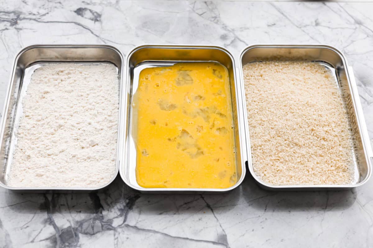 Three separate dishes with flour in one, egg mixture in another and breadcrumbs in another. 