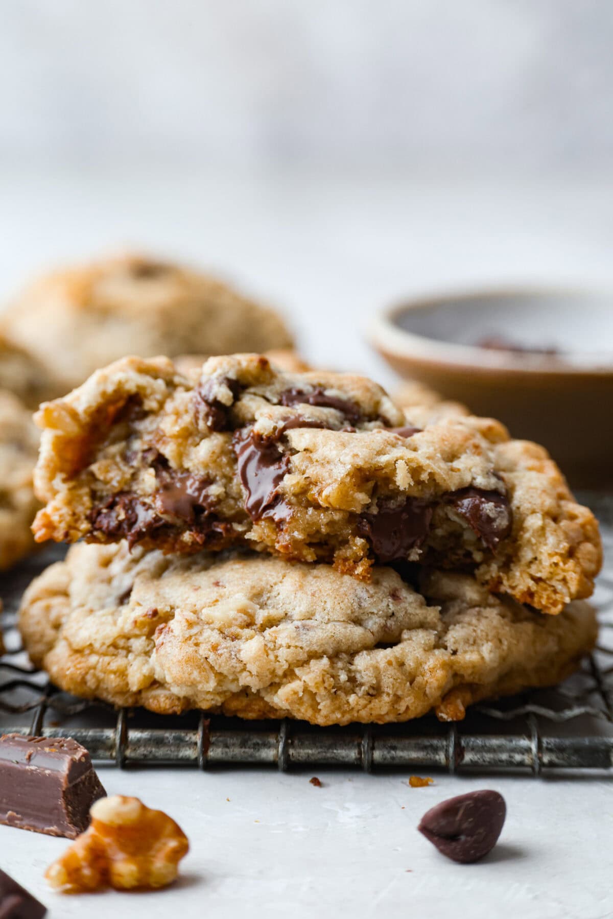 Side shot of stacked Neiman Marcus chocolate chip cookies, where the top on is cut in half and soft chocloate is melting over. 