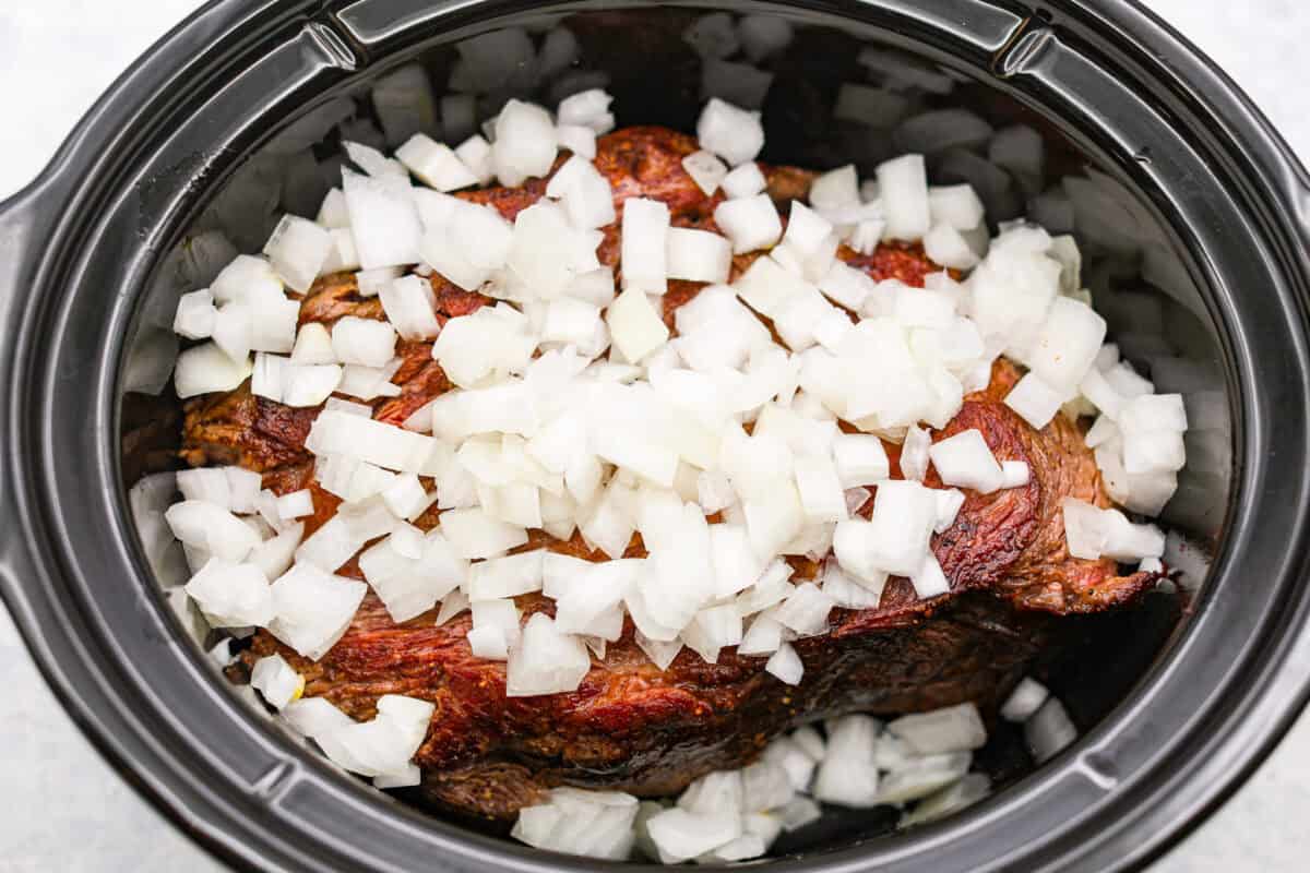 Browned pot roast in the slow cooker with diced onions.