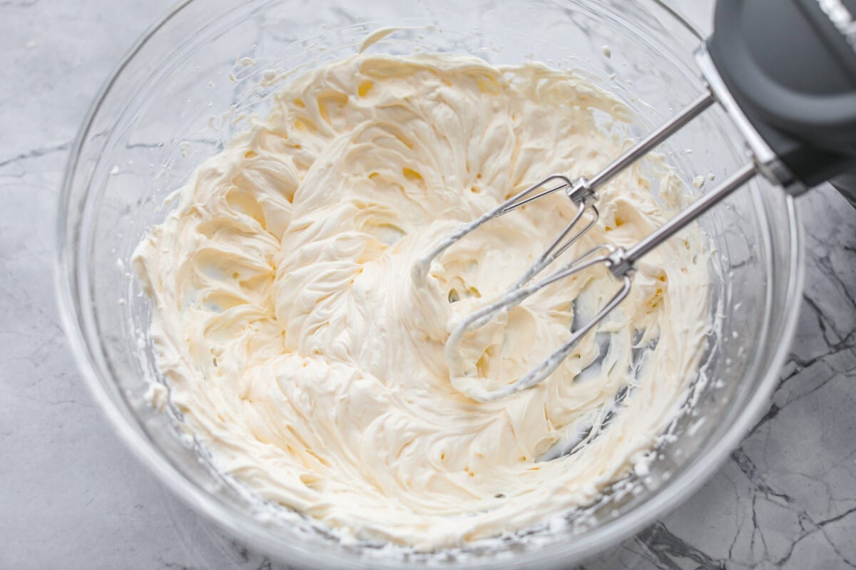 Cream cheese, sour cream, and mayonnaise all being mixed together with a hand mixer. 