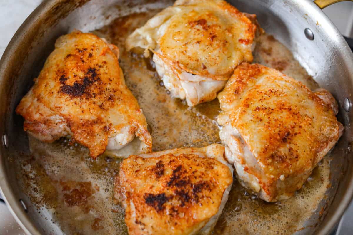 This Irish chicken is my cozy mashup of pub vibes and weeknight reality. Seared chicken thighs baked over bacon, cabbage, and potatoes, then I add a splash of Irish whiskey and a touch of cream to make the whole pan taste extra special. Chicken cooking in the bacon grease.