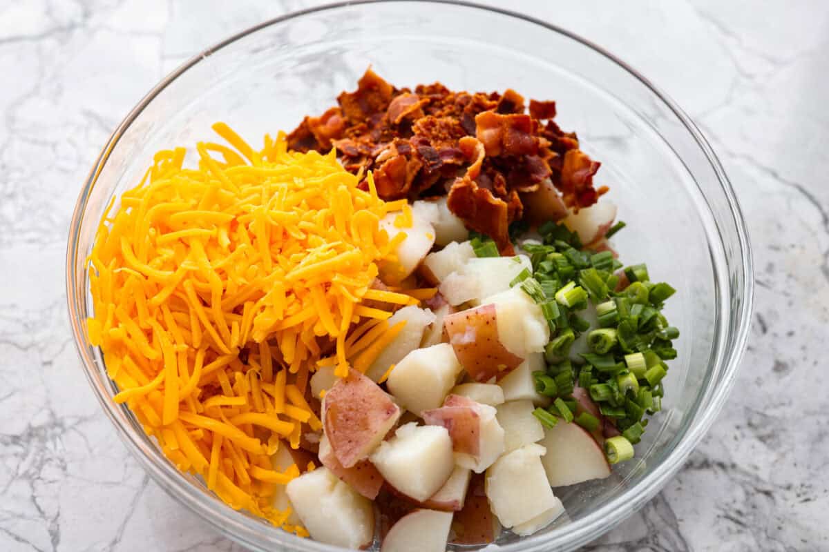 You guys have been asking, so I made the change. This Crack Potato Salad now has mayonnaise in the dressing! It seriously takes the flavors up a notch! I love the combination with the sour cream. I can't wait for you to try this new version! Cooked potatoes, cheese, green onions all added to a bowl.