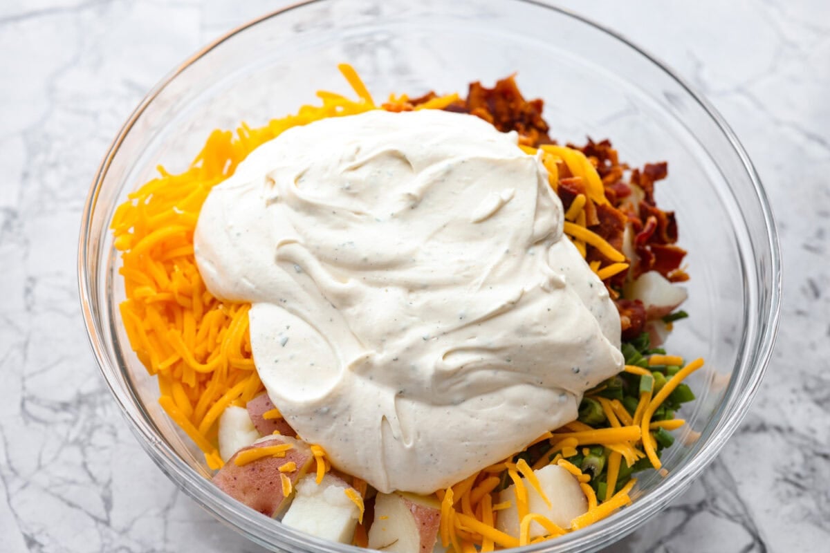 You guys have been asking, so I made the change. This Crack Potato Salad now has mayonnaise in the dressing! It seriously takes the flavors up a notch! I love the combination with the sour cream. I can't wait for you to try this new version! Sauce added to the other ingredients in the mixing bowl.