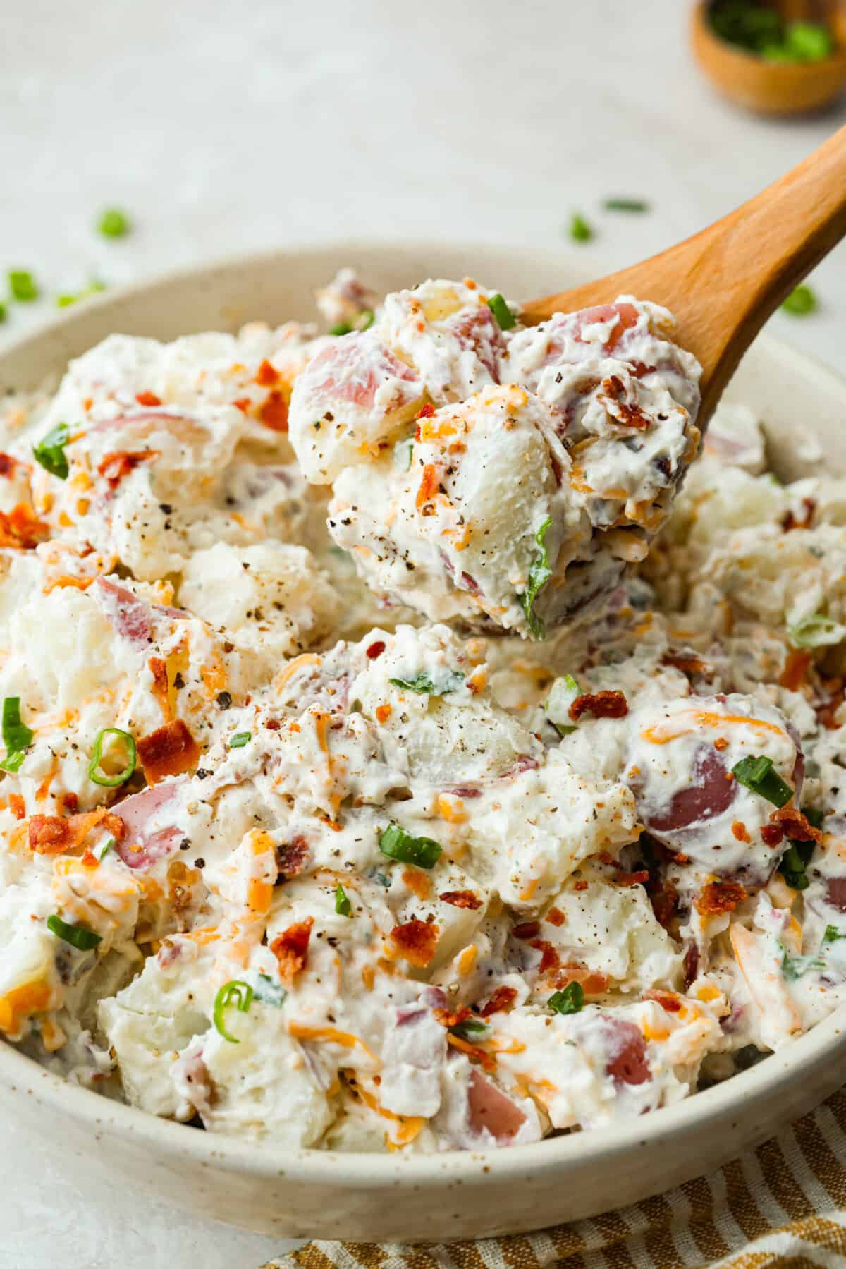 You guys have been asking, so I made the change. This Crack Potato Salad now has mayonnaise in the dressing! It seriously takes the flavors up a notch! I love the combination with the sour cream. I can't wait for you to try this new version! Angle shot of the serving bowl of crack potato salad with a wooden spoon lifting a serving out.