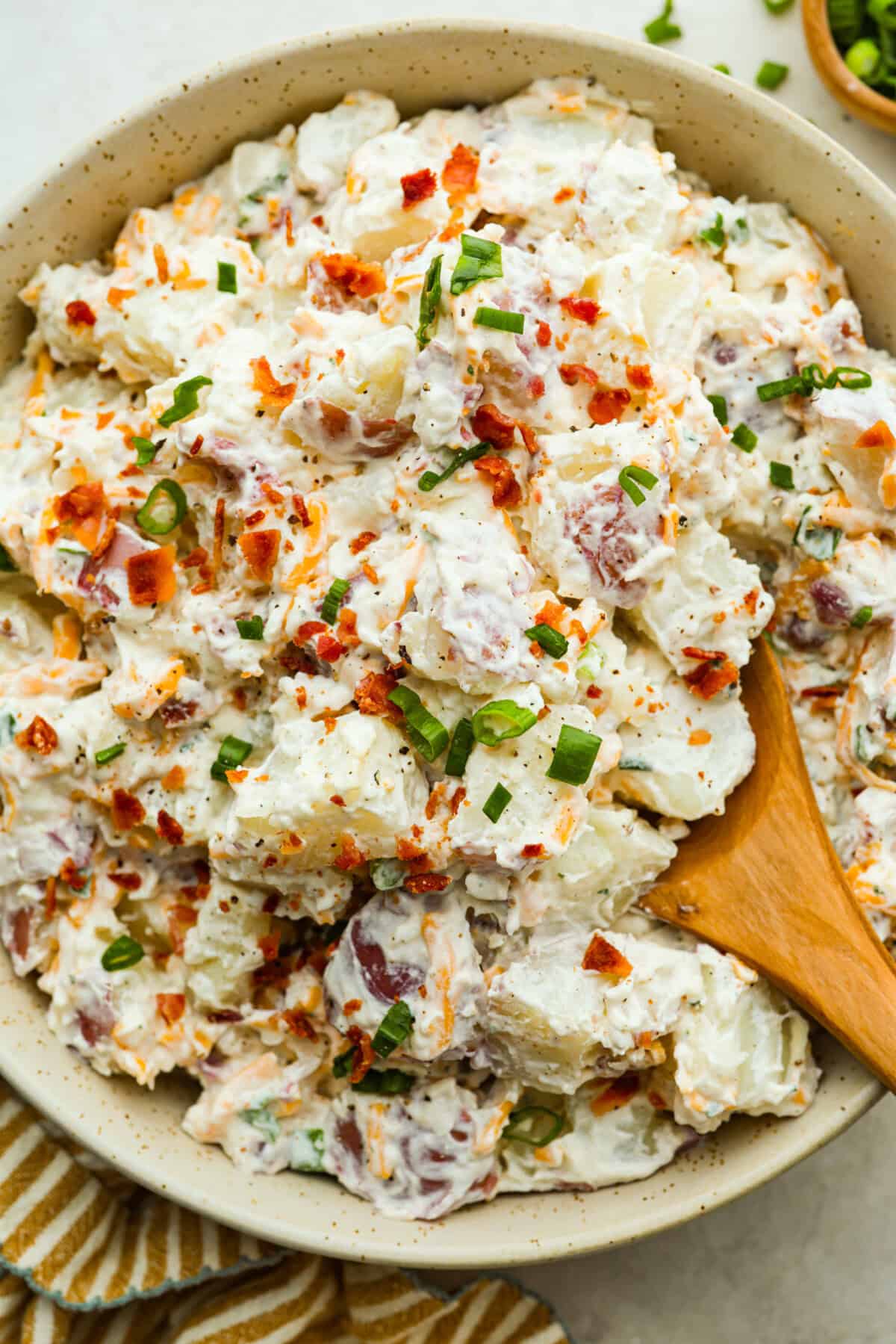 You guys have been asking, so I made the change. This Crack Potato Salad now has mayonnaise in the dressing! It seriously takes the flavors up a notch! I love the combination with the sour cream. I can't wait for you to try this new version! Close up shot of a bowl of crack potato salad with wooden spoon.
