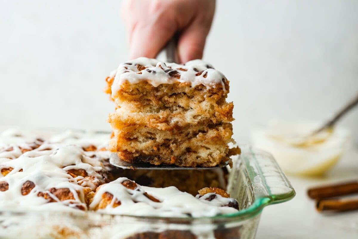 someone lifting a piece of cinnamon roll butter swim biscuit out of the pan.