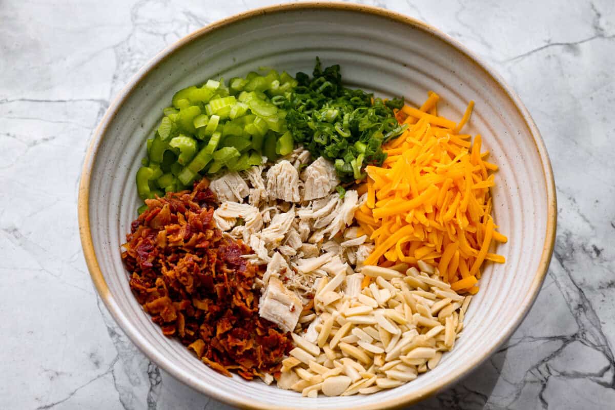 Chicken, bacon, celery, green onions, cheese and almonds all added to a bowl.