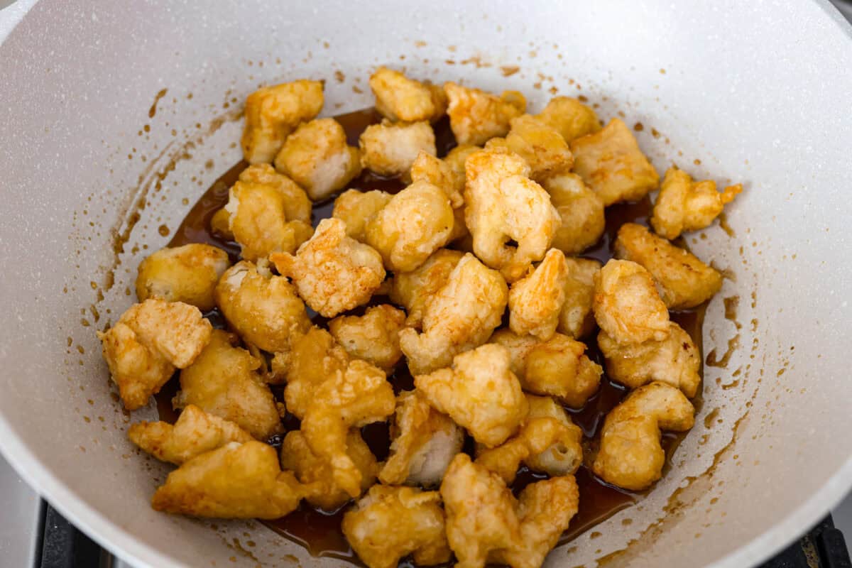 Fried chicken pieces added to the sauce in the wok. 