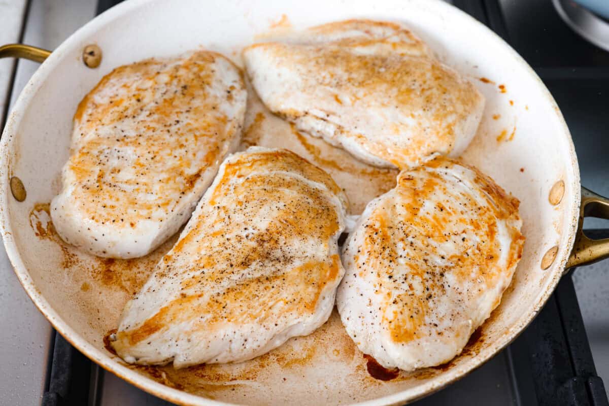 Chicken breasts cooking in a skillet.