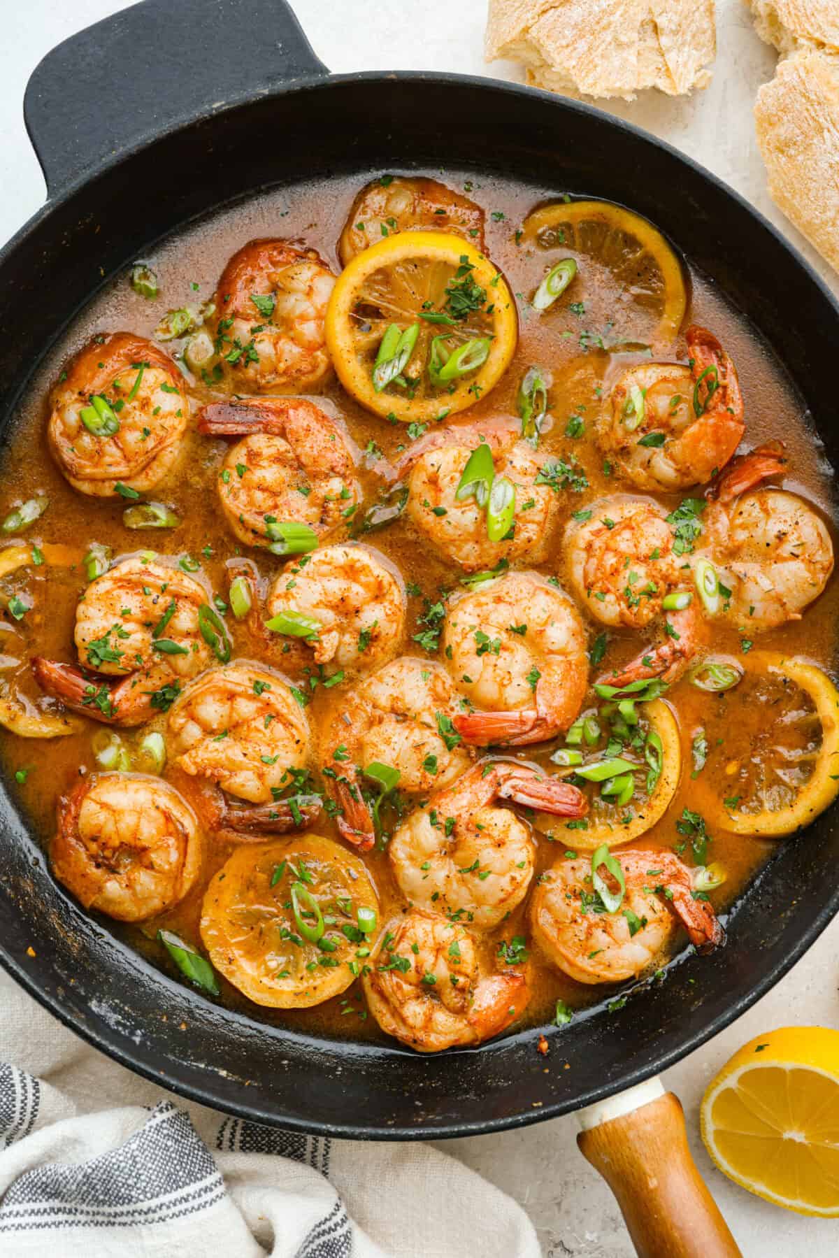 Cooked and garnished New Orleans BBQ shrimp in a skillet. 